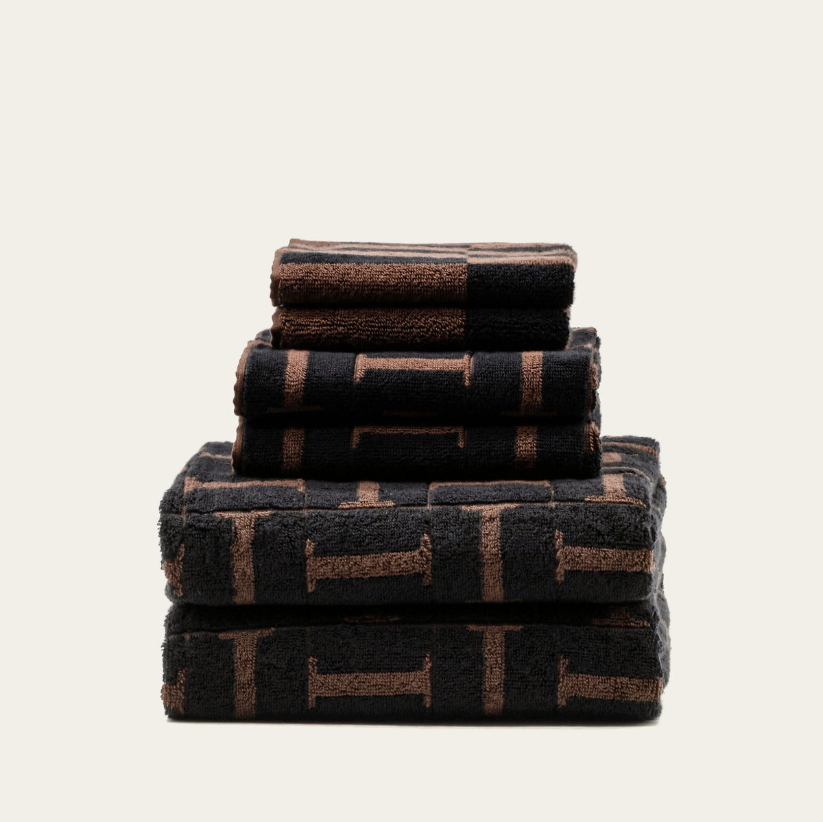 Stack of folded terry cotton towels in tobacco and black with woven geometric pattern