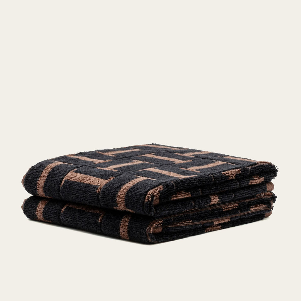 Folded terry cotton towels in tobacco and black with woven geometric design, side view
