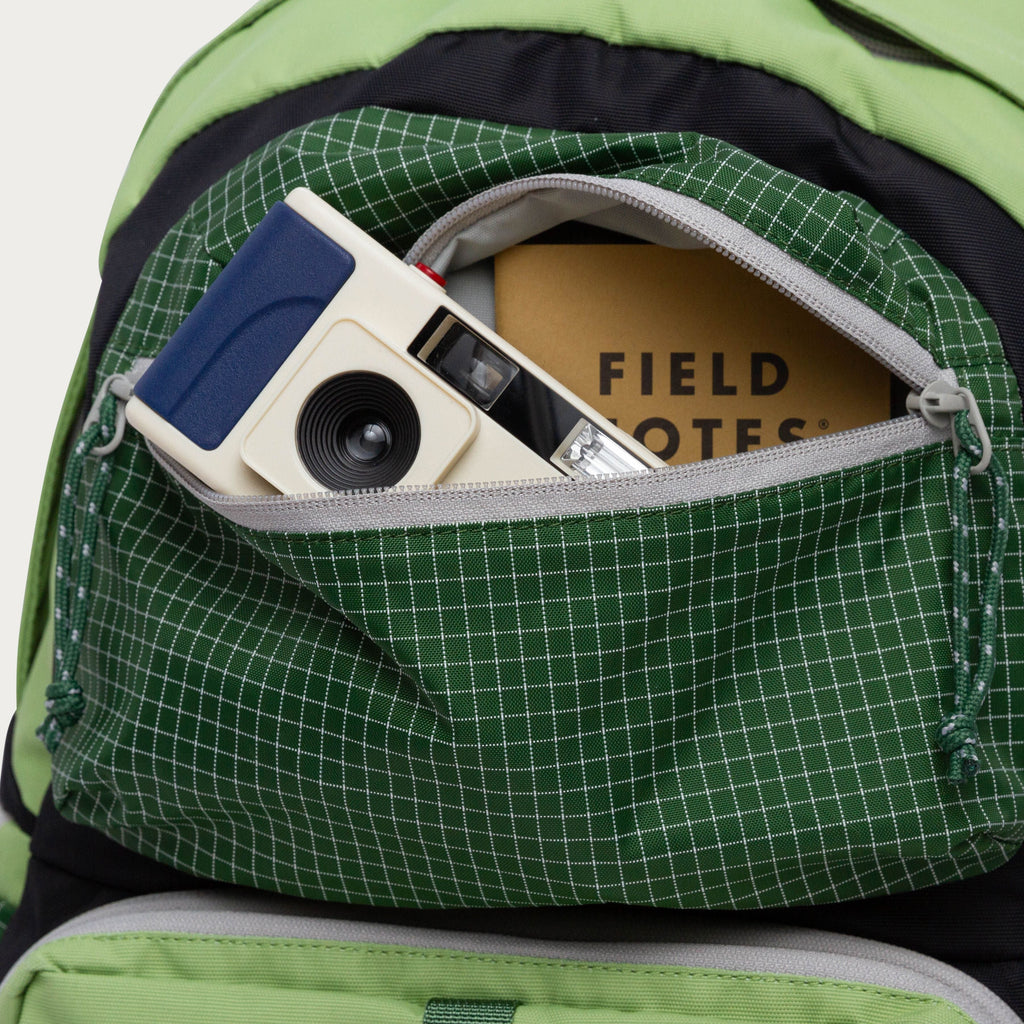 Close-up of moss green backpack pocket with camera and grid-pattern lining