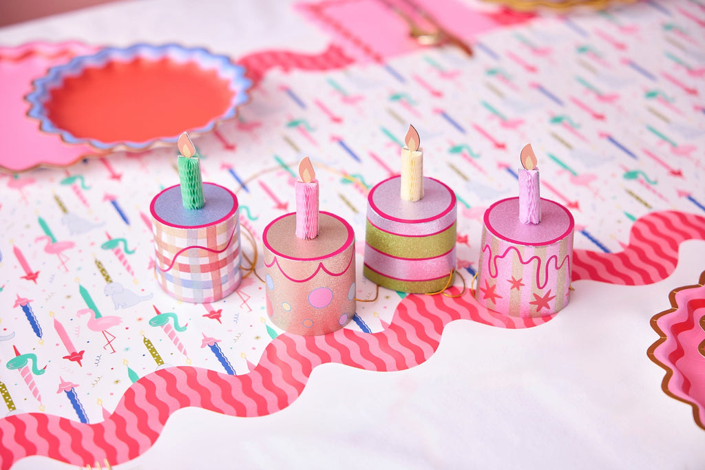 Mini birthday cake party hat set on table, four mini cylindrical hats with candle flames
