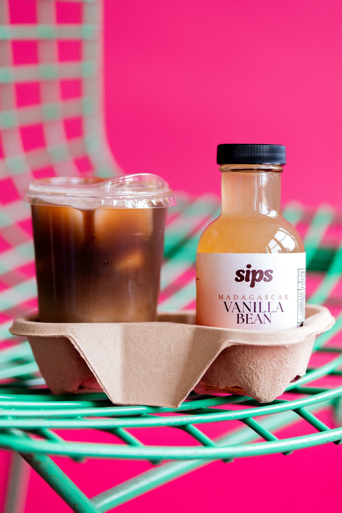 Vanilla bean coffee syrup bottle beside iced drink in paper holder, Sips label.