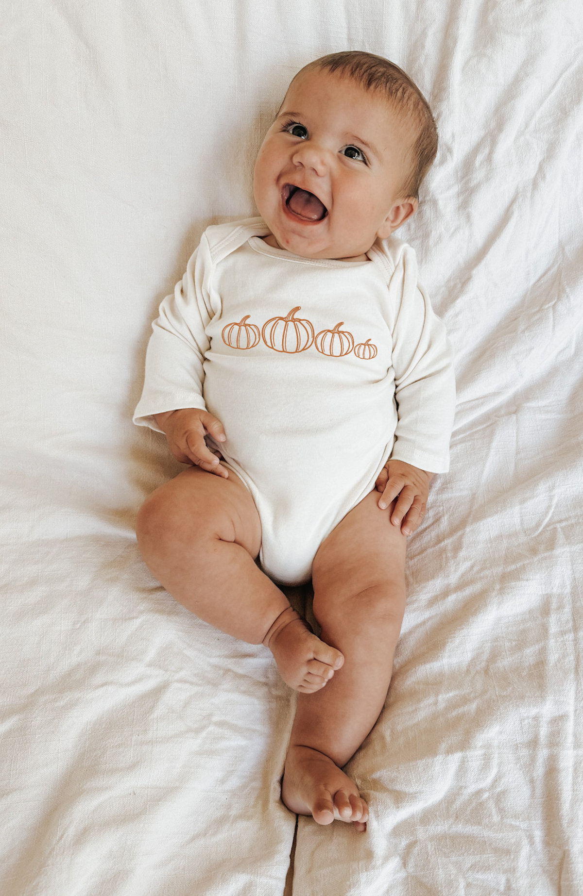 Cream long-sleeve bodysuit with orange pumpkin print on baby with arms up