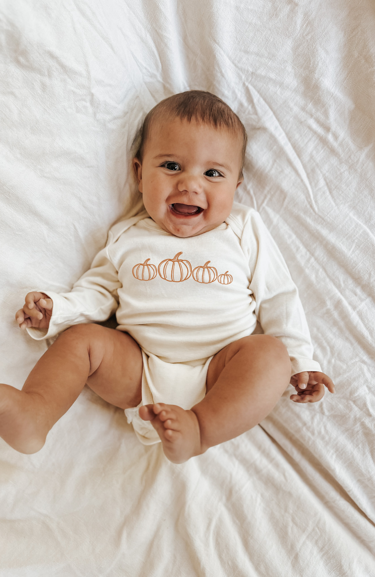 Cream long-sleeve bodysuit with orange pumpkin print, worn by smiling baby