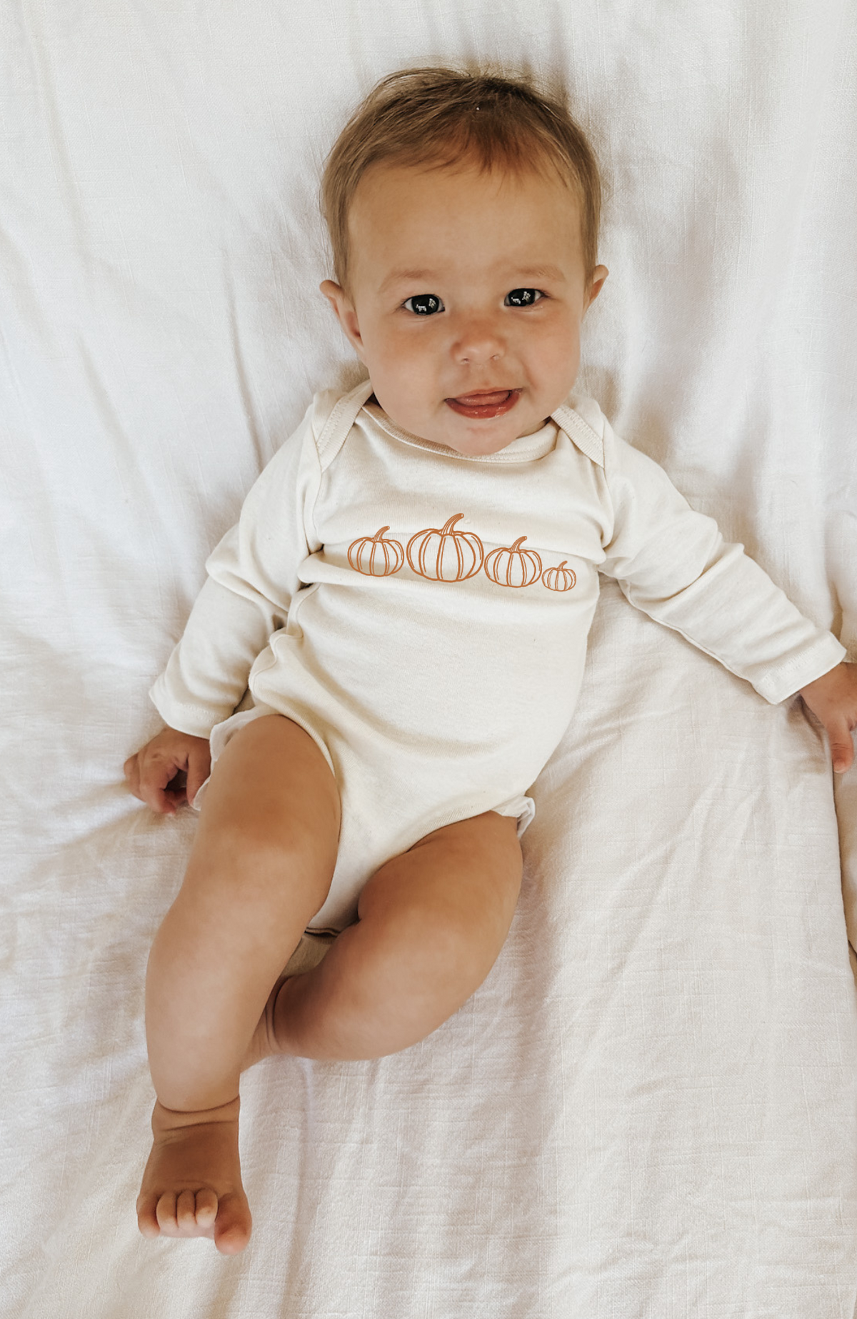 Cream long-sleeve bodysuit with orange pumpkin print on seated baby