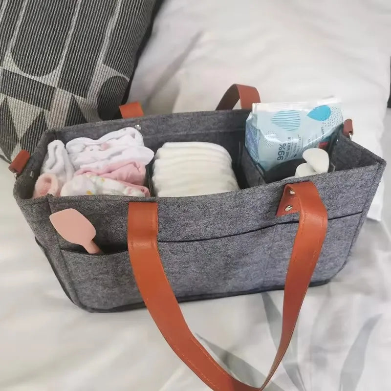 Grey felt storage basket organizer with brown handles holding baby supplies and wipes