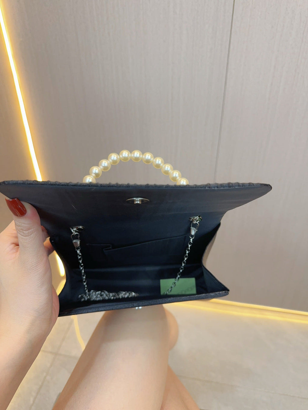 Dark pleated clutch bag open, showing satin-lined interior and pearl handle