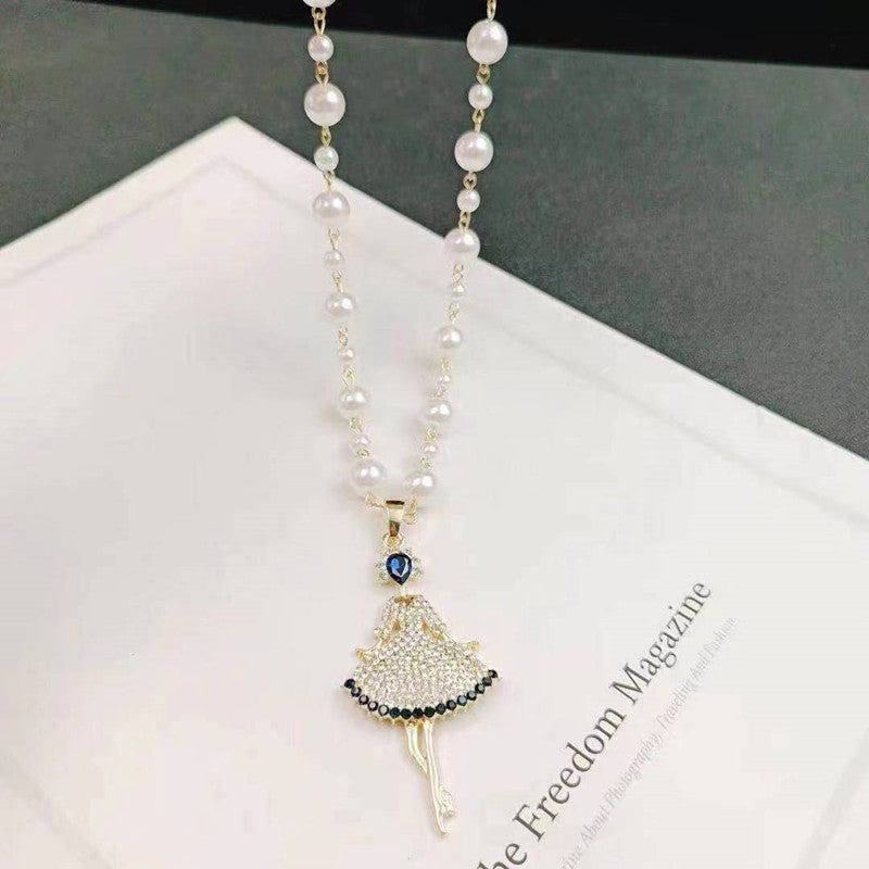 Long pearl necklace with gold dress-like pendant, small blue stone, and dangling pearls