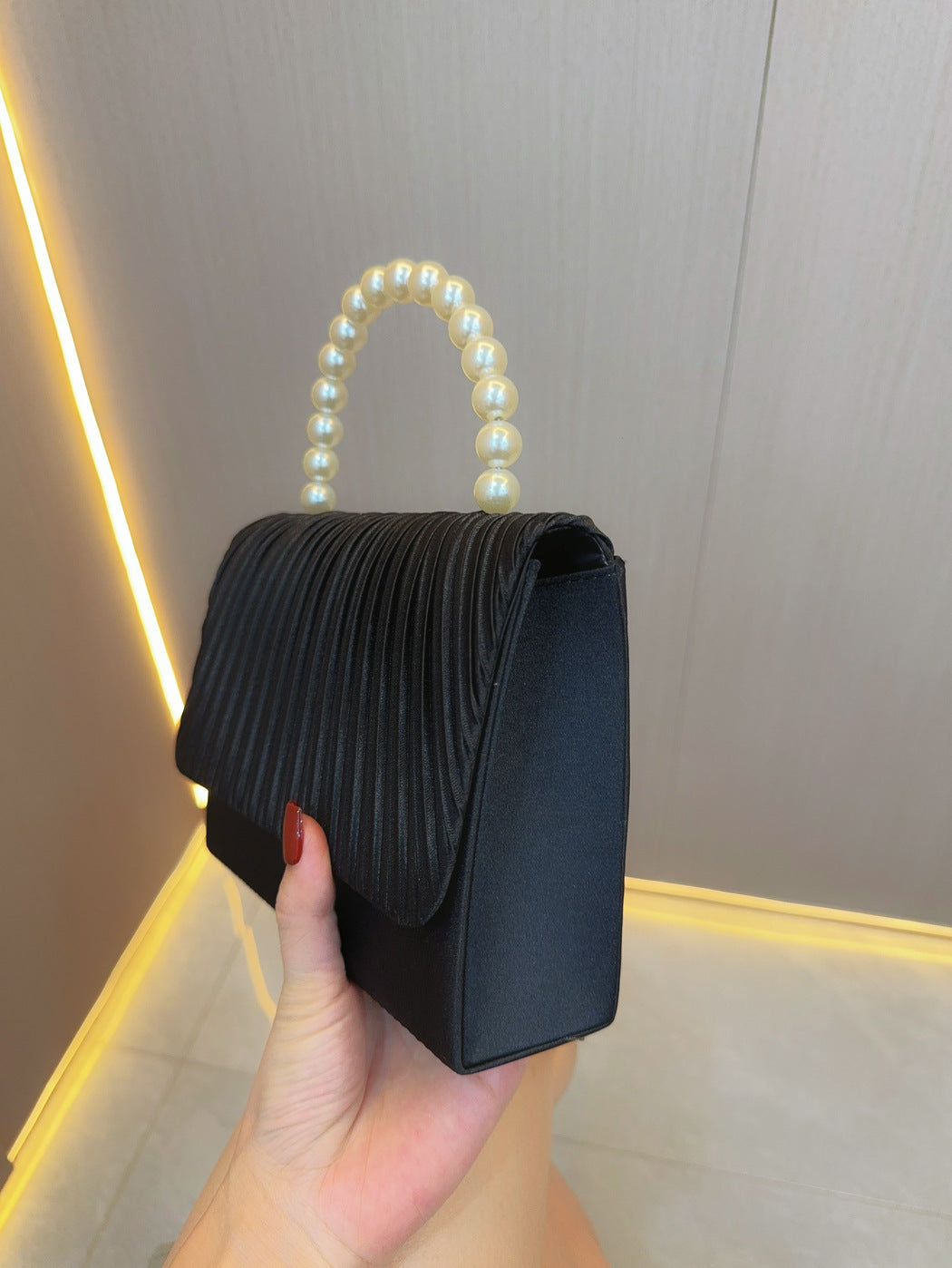 Dark pleated crossbody clutch with faux pearl handle, side view