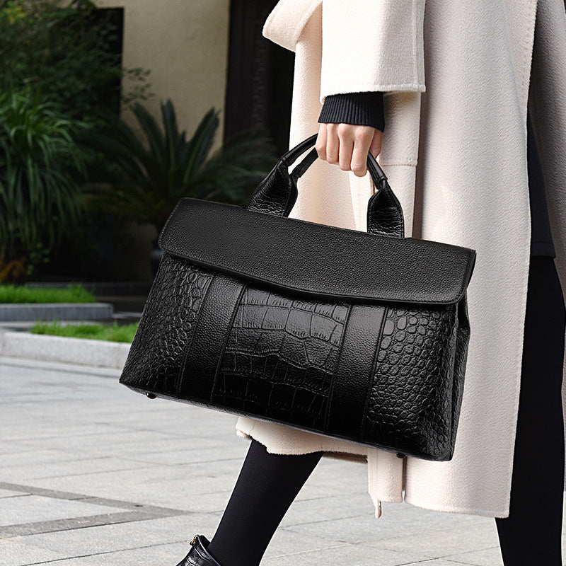 Black embossed handbag with top handle and shoulder strap, flap closure