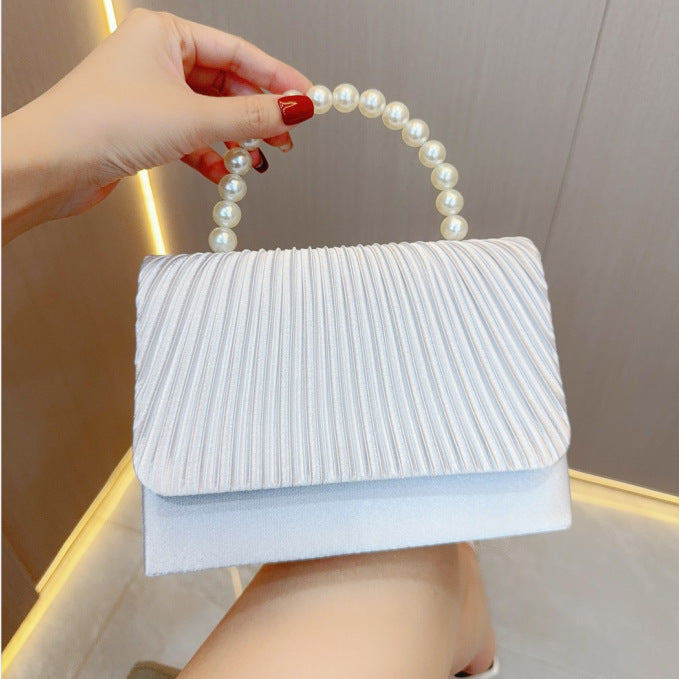 White pleated crossbody clutch with faux pearl handle and fold-over flap