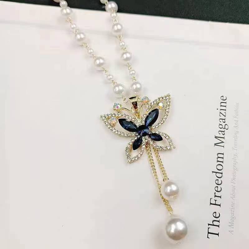 Long pearl necklace with rhinestone flower cross pendant, blue accents, and pearl drops