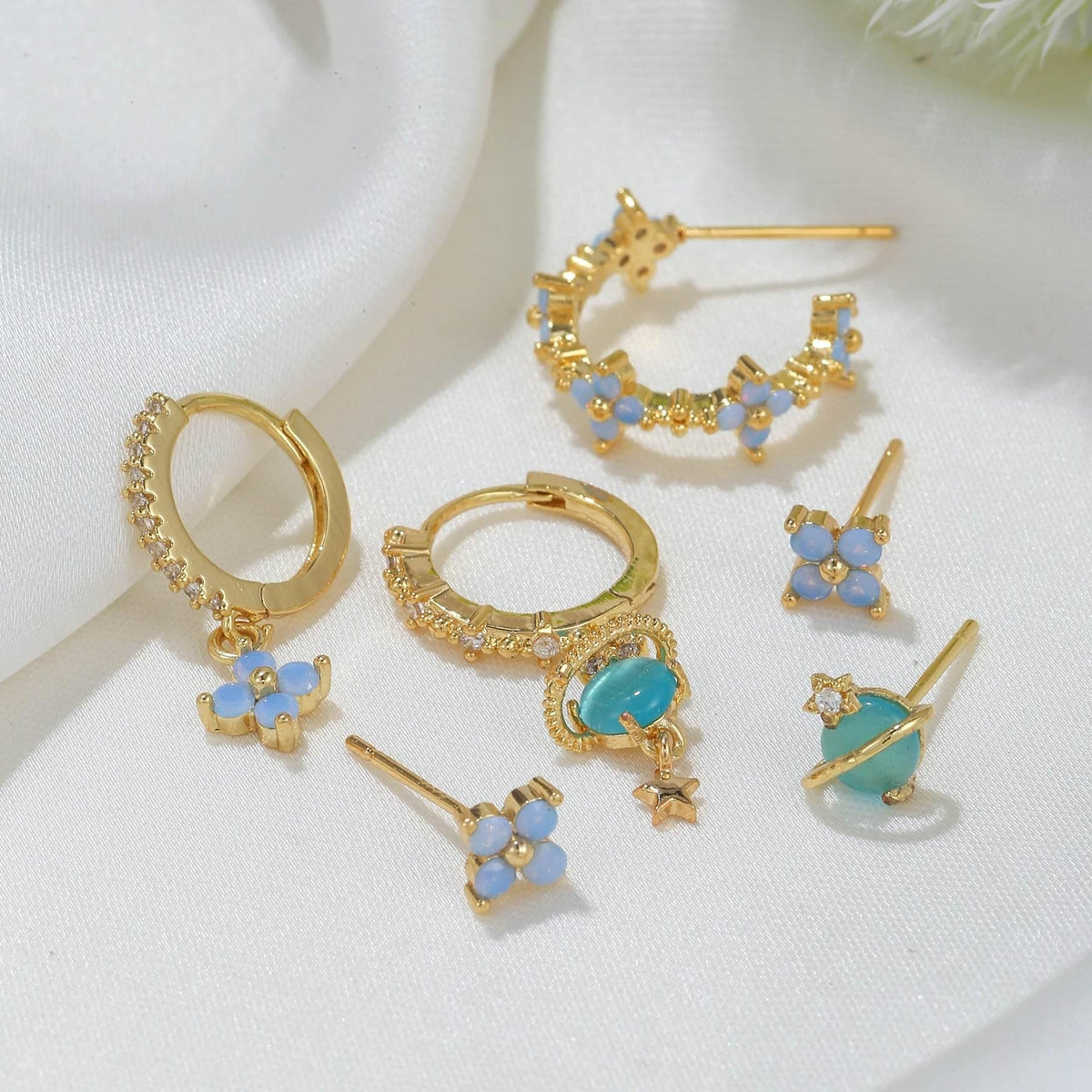 Gold-tone stacking earring set with blue flower charms, teal drops, and zircon details