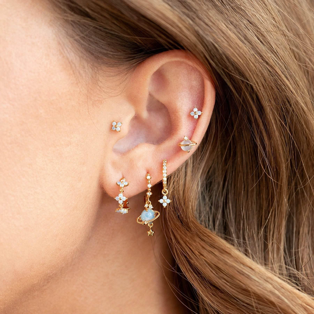 Stackable blue flower and teal drop earrings shown on ear with gold-tone hoops