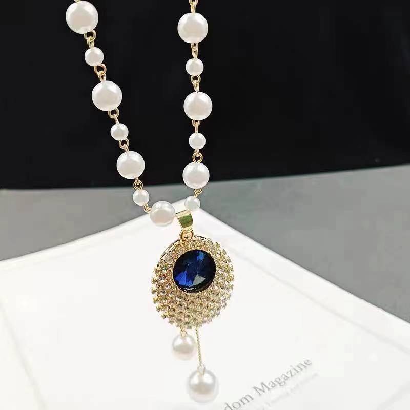 Long pearl beaded necklace with gold hoop pendant featuring a blue oval stone and pearls