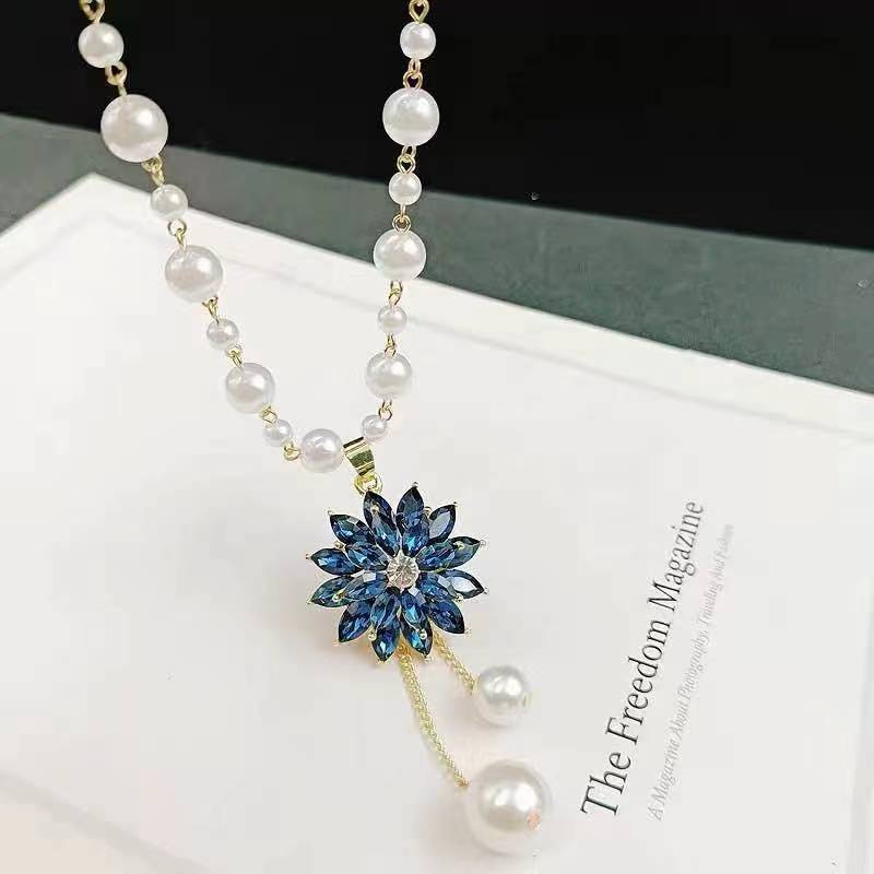 Long pearl necklace with blue flower pendant, gold stem, and dangling pearl drops