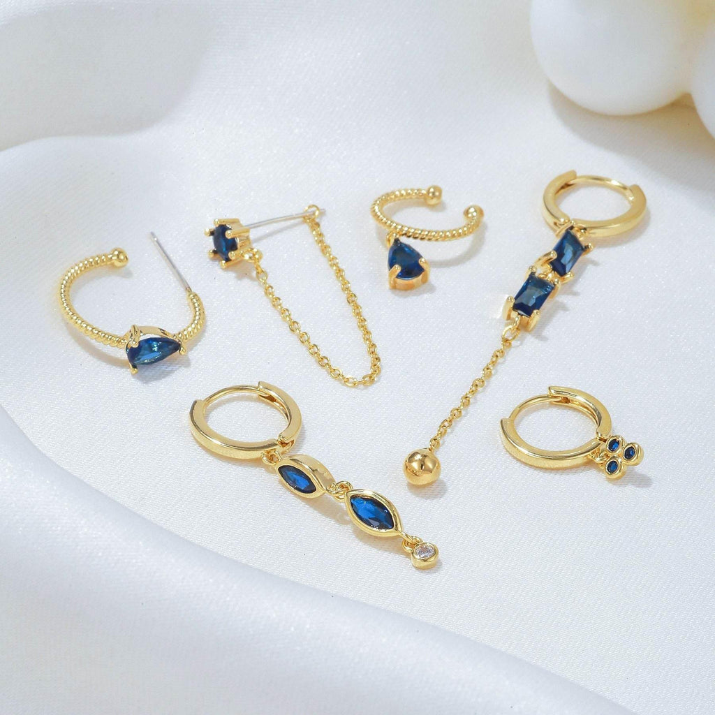 Gold-tone earrings set with blue teardrop stones and small hoop and drop styles
