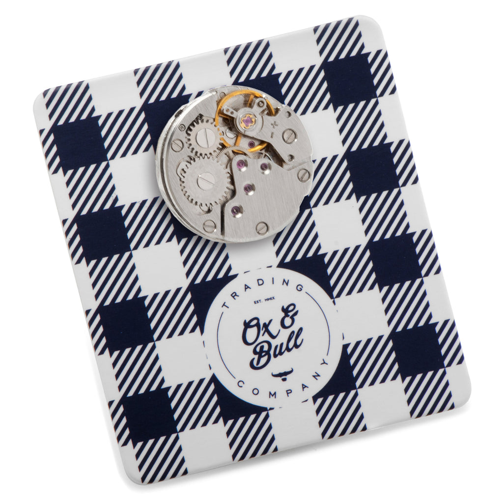 Circular skeleton watch-movement lapel pin on a plaid display card