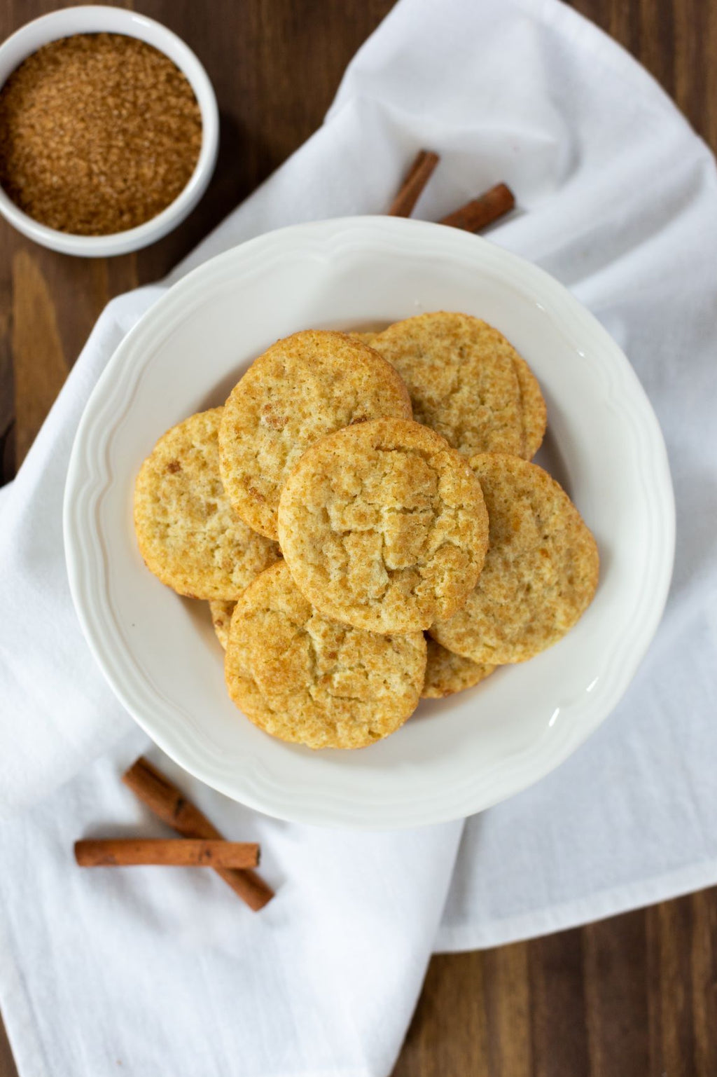 Snickerdoodle cookie mix beside a bowl of round snickerdoodle cookies and cinnamon sticks