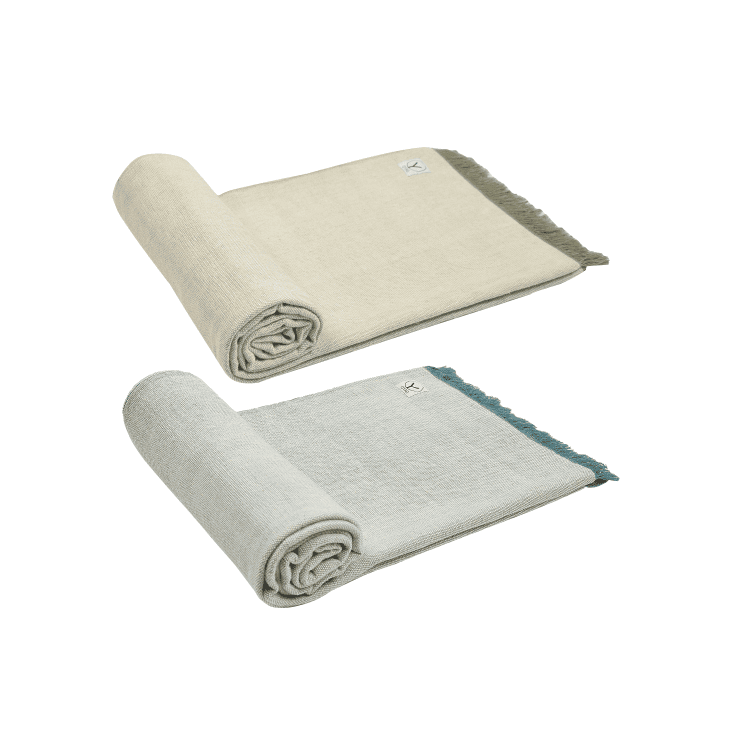 Light green organic cotton yoga blanket, folded with rolled ends and corner emblem.