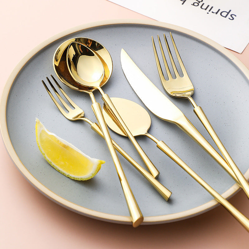 Gold cutlery set on a round tray: spoon, fork, and knife with lemon garnish