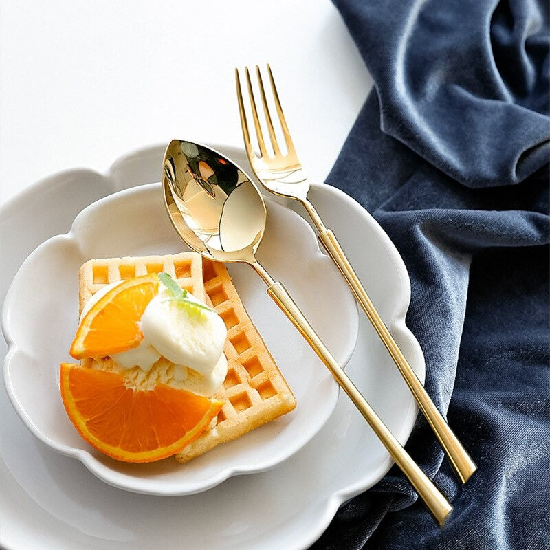 Gold cutlery set with spoon and fork beside a waffle with fruit