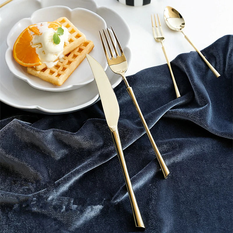 Gold cutlery set with knife, fork, and spoon on a plate and dark cloth