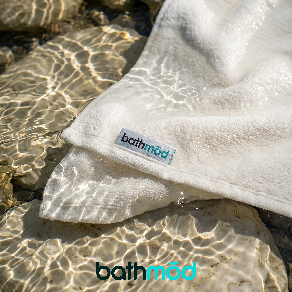 White organic bath sheet with Bathmod logo, folded on natural stone