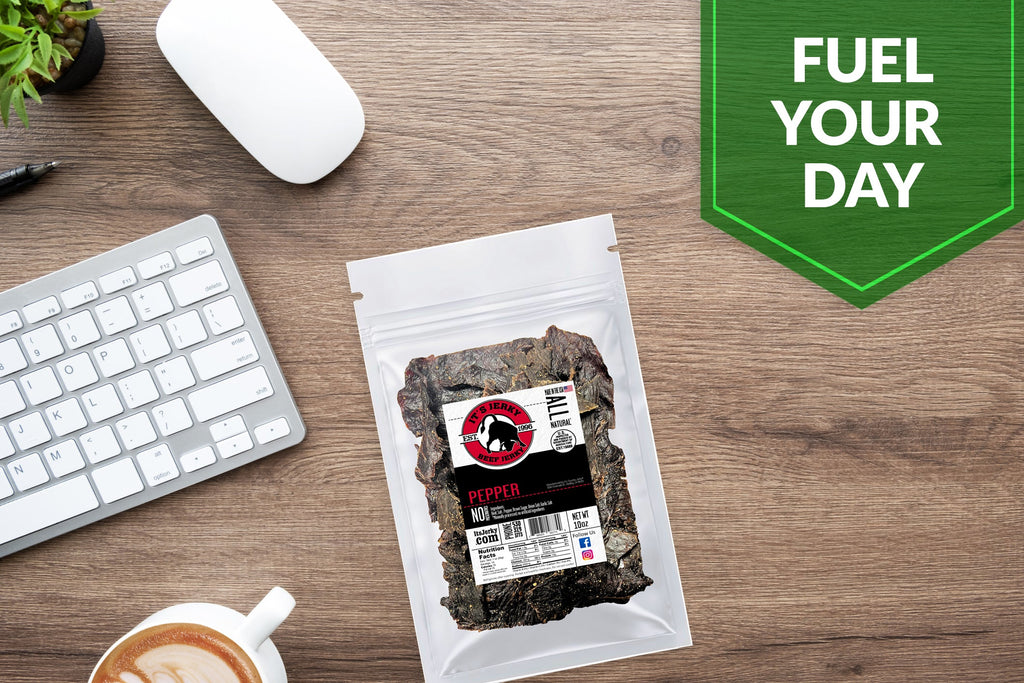 Pepper beef jerky pouch on a wooden table near a keyboard and coffee.