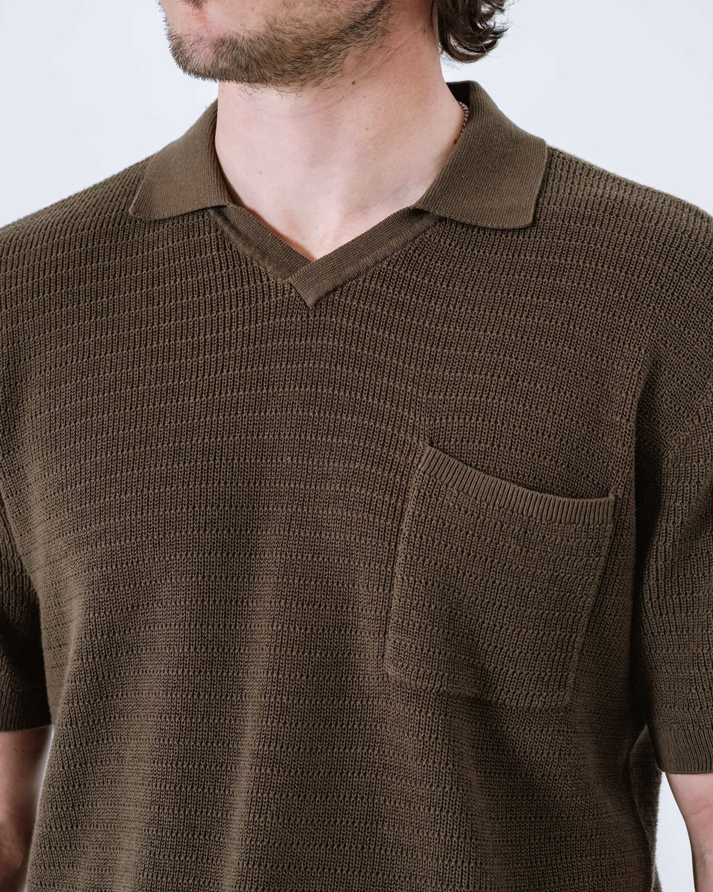 Men's dark-brown knit golf polo close-up: textured knit and chest pocket.