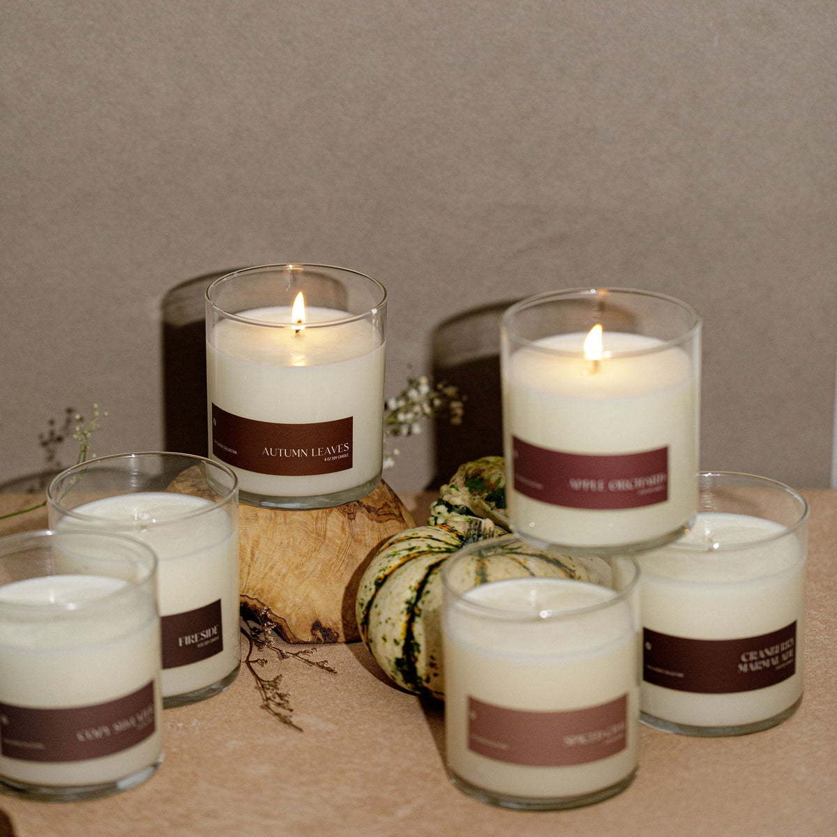 Lit soy candles in clear glass jars with brown labels and white wax, flames visible