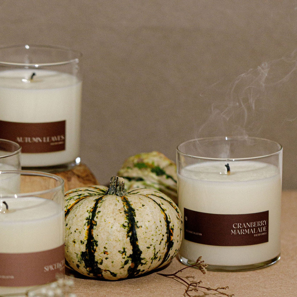Soy candle jar with brown label and white wax, clear glass; small pumpkin nearby