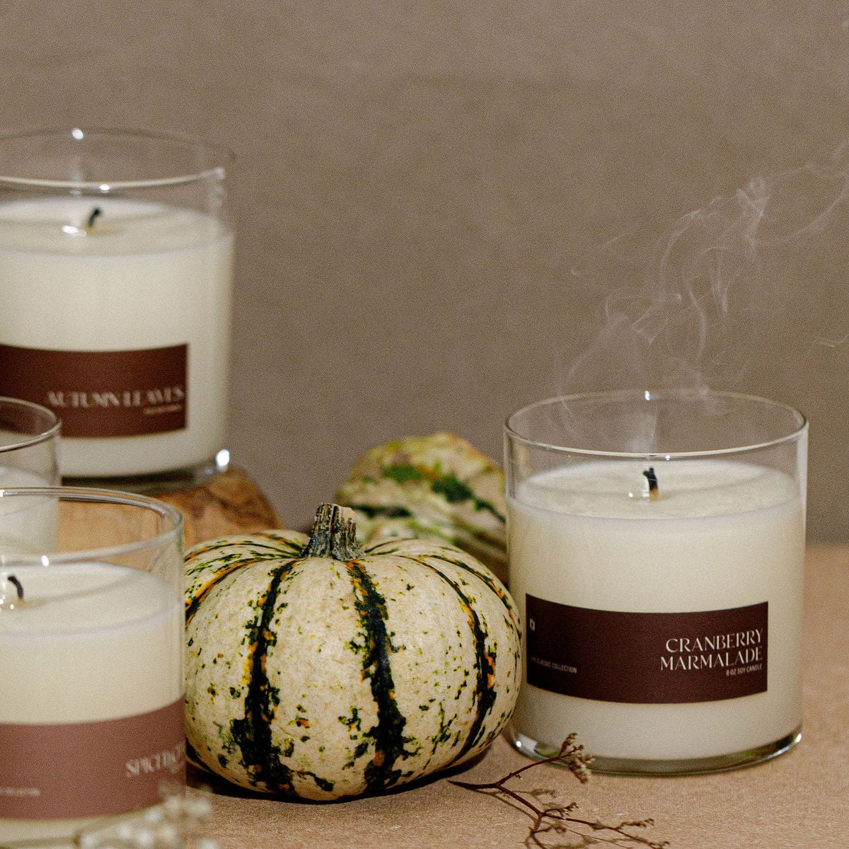 Soy candle jar with brown label and white wax, clear glass; small pumpkin nearby