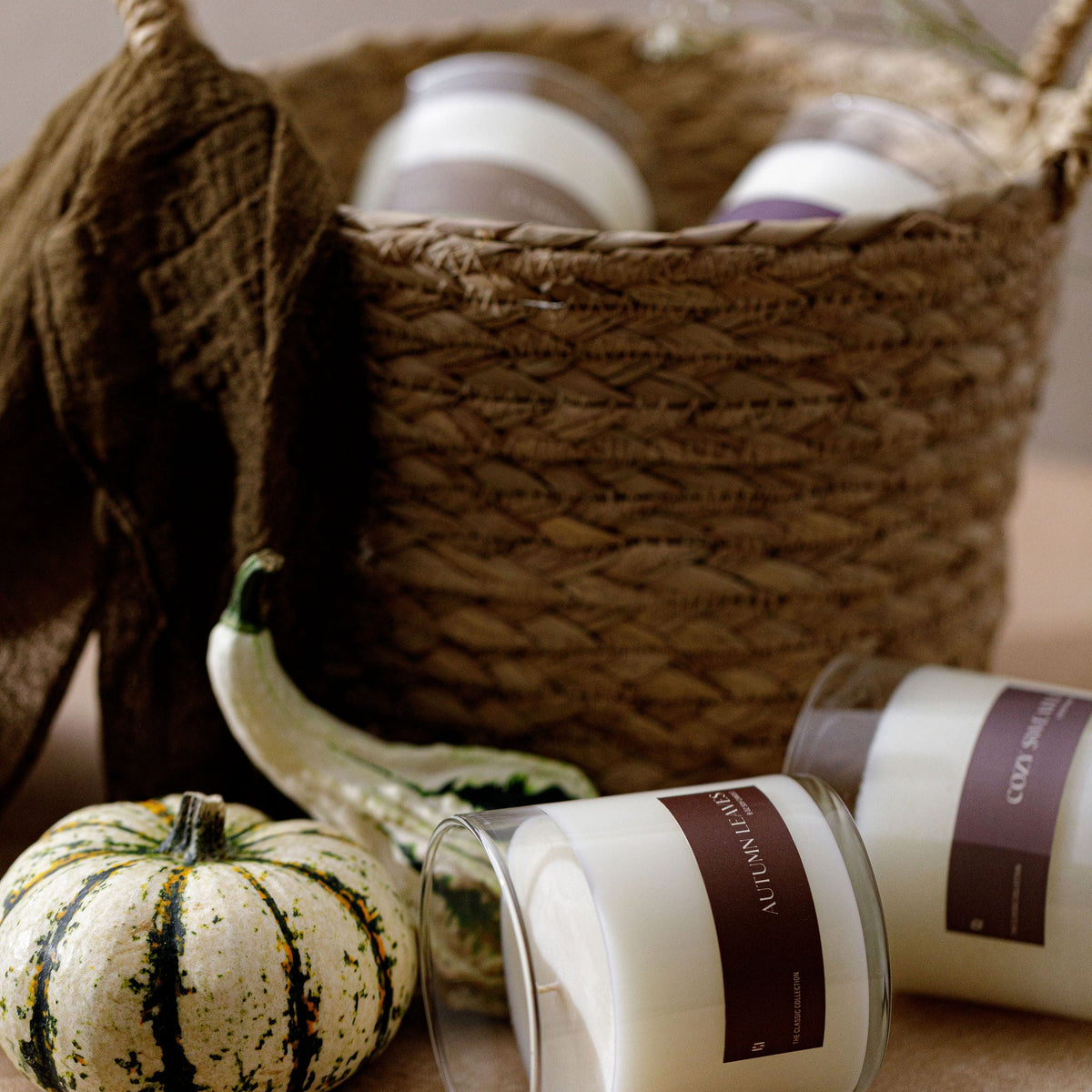 Soy candle jars with brown labels beside small pumpkins in a woven basket