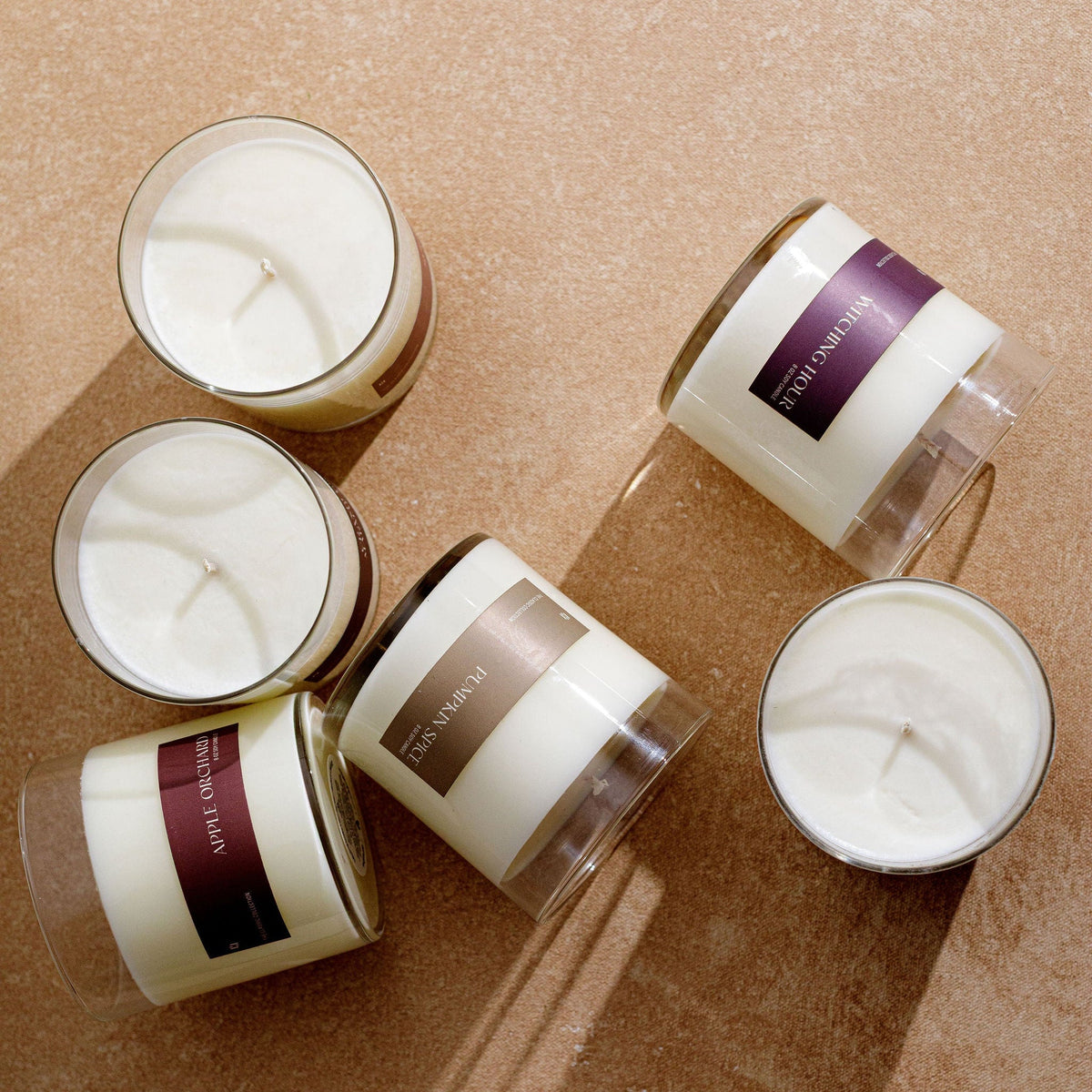 Set of soy candles in clear glass jars with brown labels and white wax, on textured surface