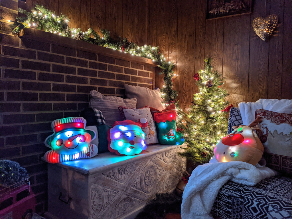 Two glowing LED Christmas stocking pillows on a bench near holiday decorations