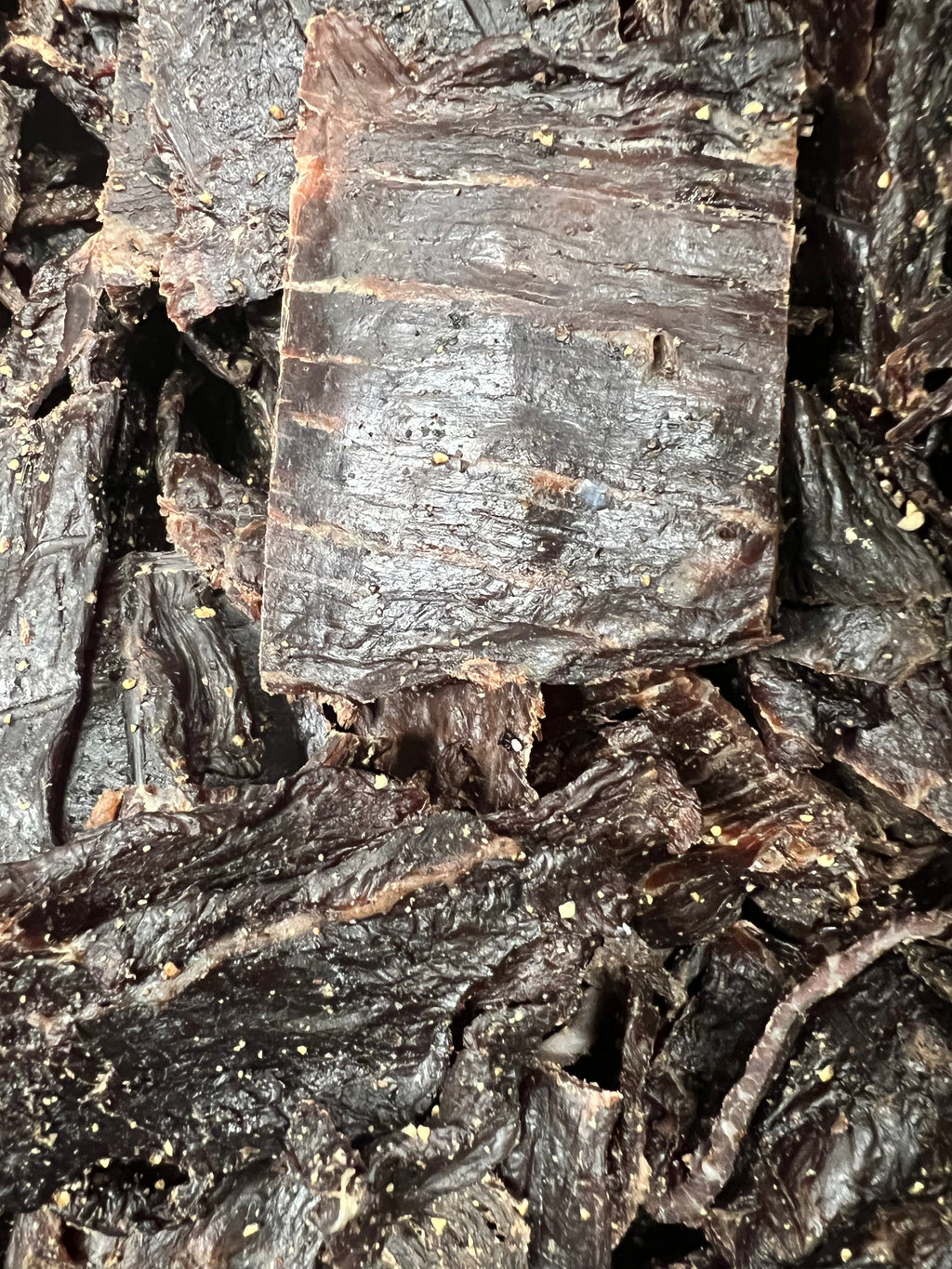 Pepper beef jerky pieces with dark brown, fibrous, peppered texture.