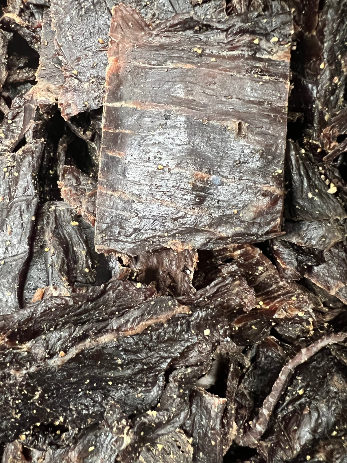 Pepper beef jerky pieces with dark brown, fibrous, peppered texture.