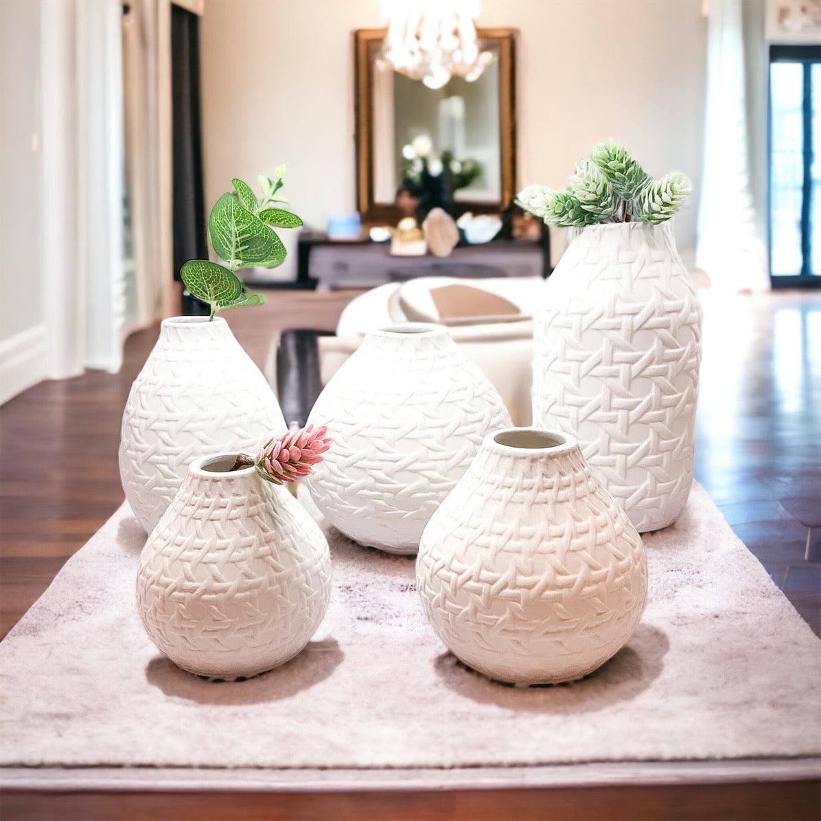 White textured web-pattern vases with green stems, arranged on a soft runner