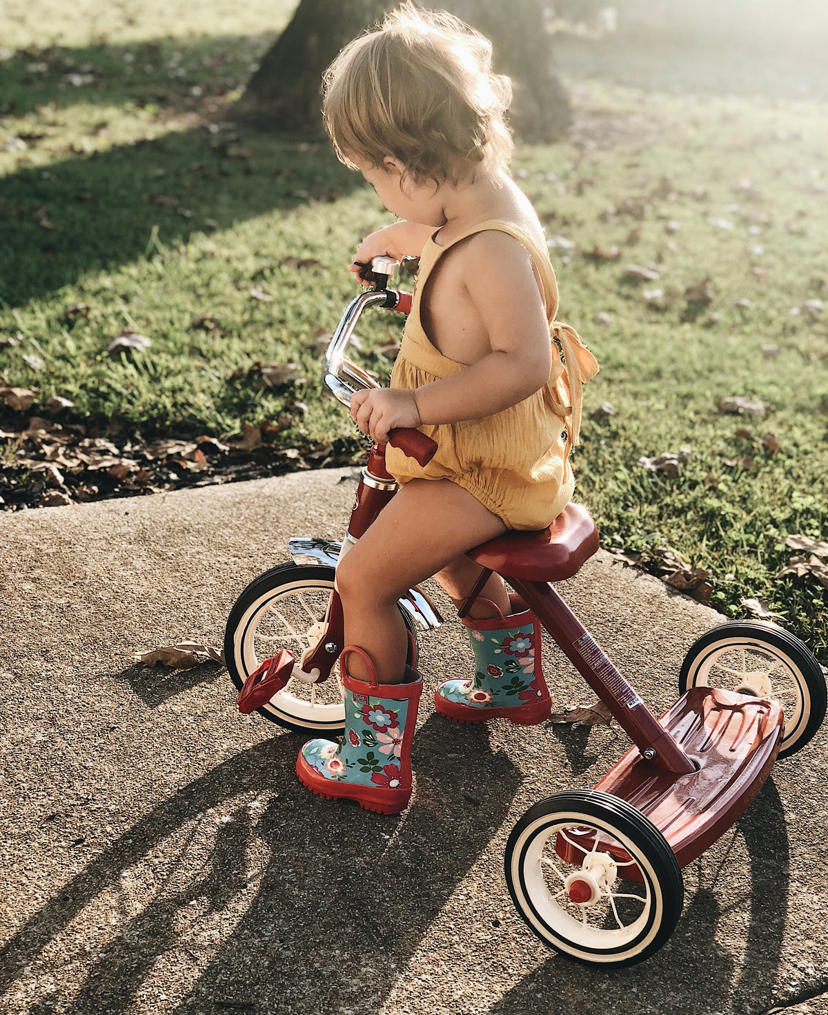 Teal floral rain boots with red trim on child’s feet while sitting outdoors