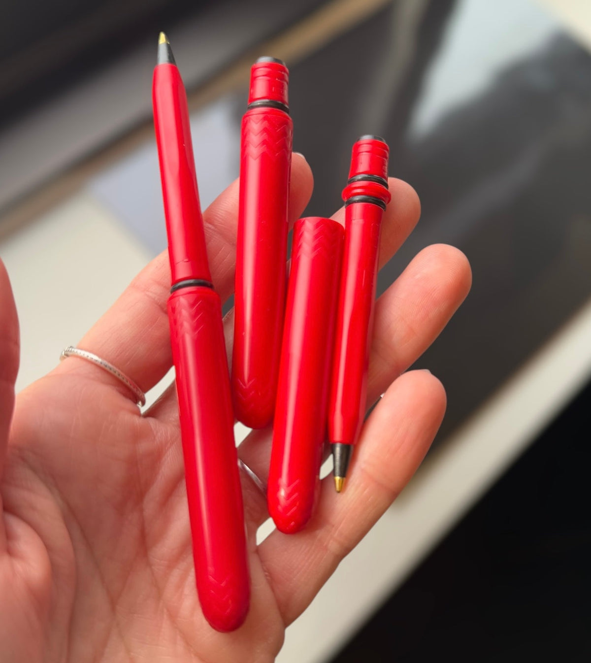 Cardinal red pocket pens held in hand, black tips and ribbed barrels