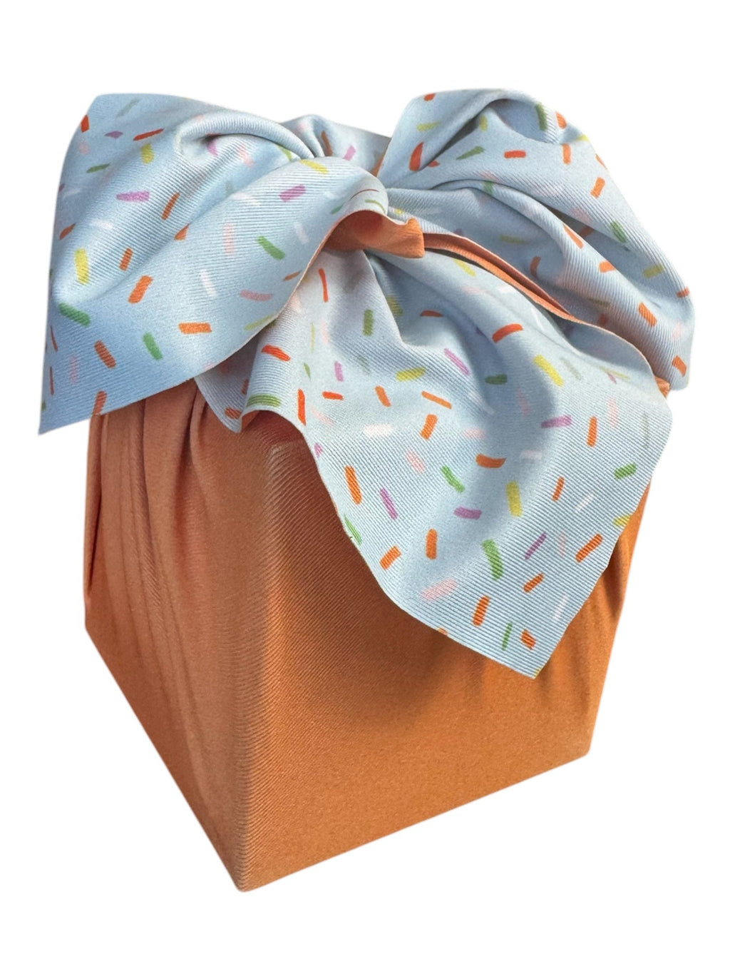Light blue sprinkle-pattern reusable furoshiki wrap with tied bow over brown panel