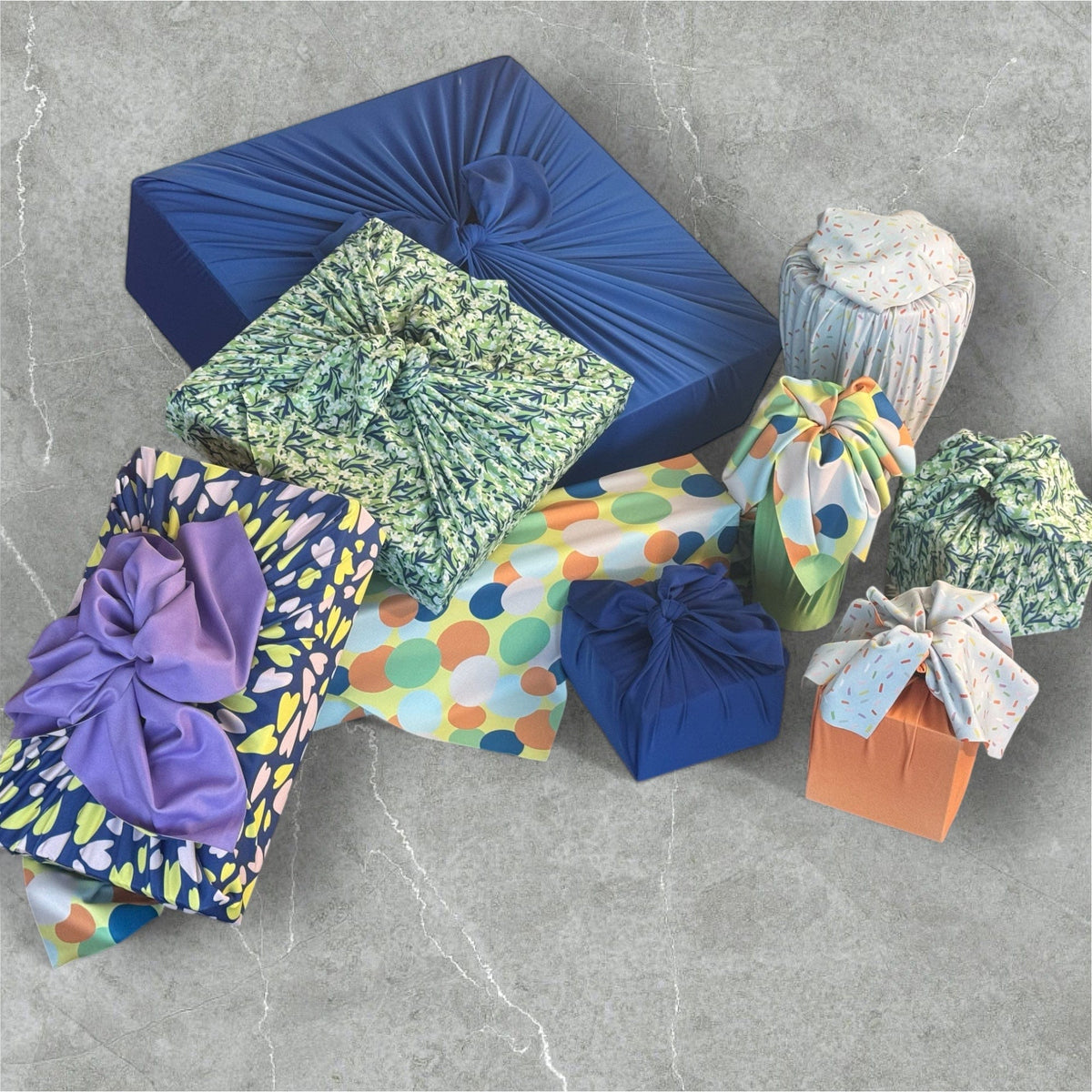 Nine reusable cloth furoshiki wraps with blue, green, purple, and multicolor patterns, tied bows