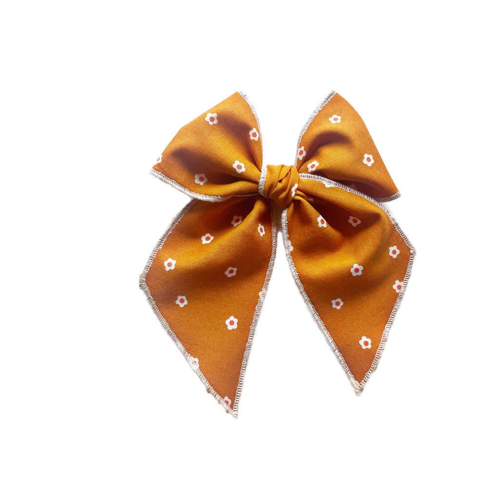 Caramel orange bow with white posie print, centered knot, and zigzag stitched edges