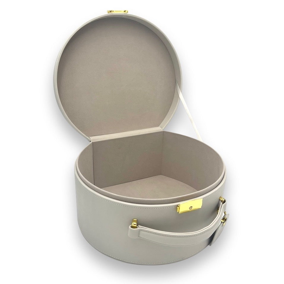 Gray round keepsake box open with beige interior and gold-tone clasp and strap