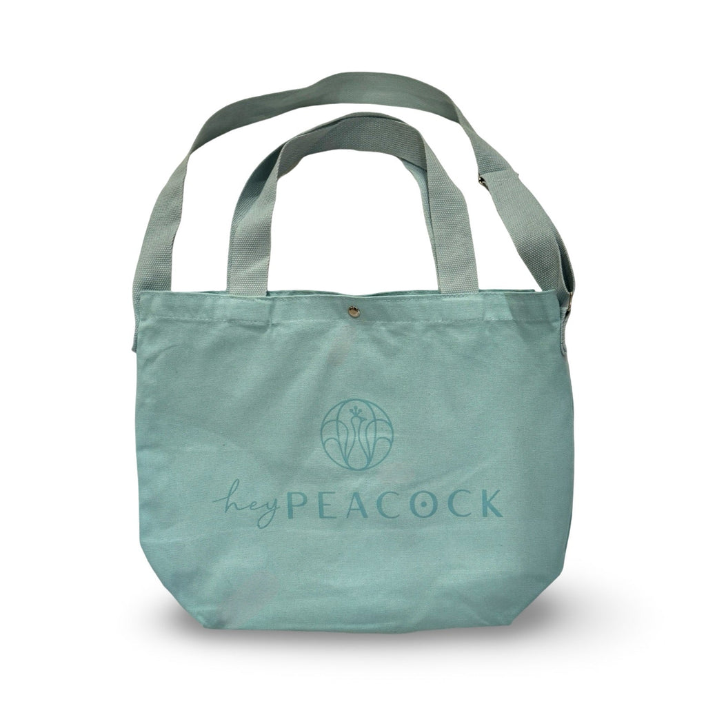 Aqua canvas tote bag with two handles and heyPEACOCK logo on front