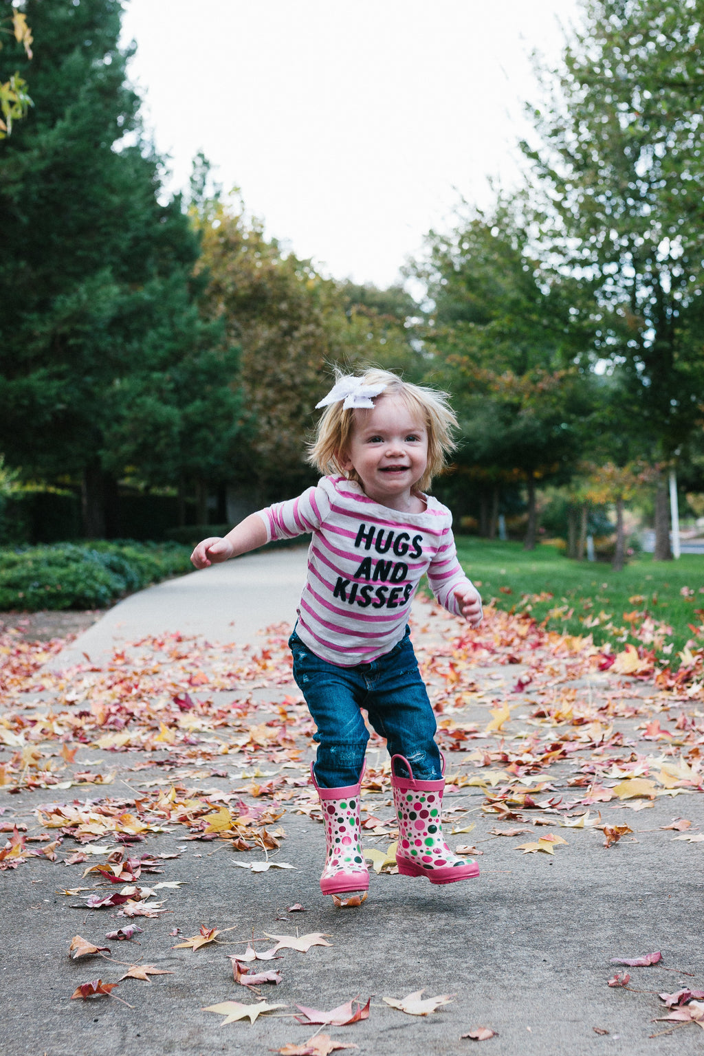 Pink kids rain boots with multicolor dot print, worn on outdoor pavement