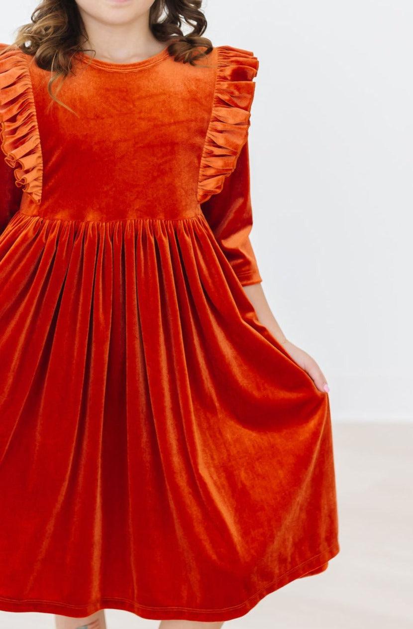 Orange velvet dress close-up: ruffled shoulders and gathered skirt flare