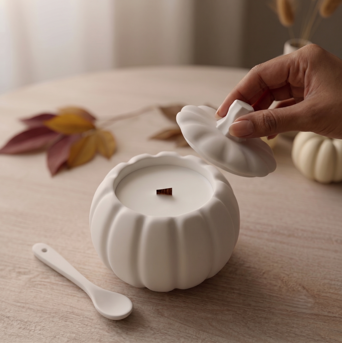 Hand placing removable lid on white pumpkin-shaped candle with ridged design