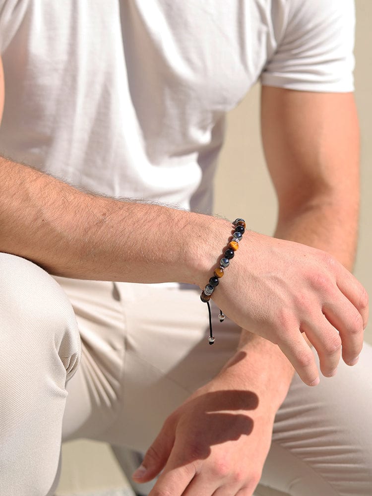 Beaded bracelet on wrist with black and gold round beads and braided cord ties