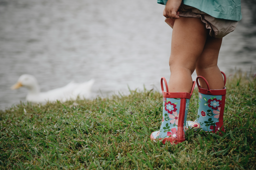 Teal floral rain boots with red trim on a child’s lower legs